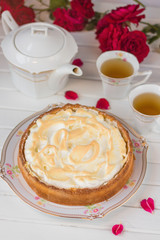 Meringue pie on a white table near teapot and cups and red roses.