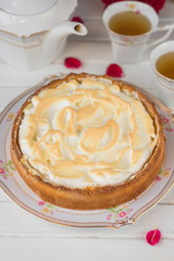 Meringue pie on a white table near teapot and cups and red roses.