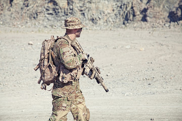 Location shot of soldier in field uniforms with rifle in the desert among rocks