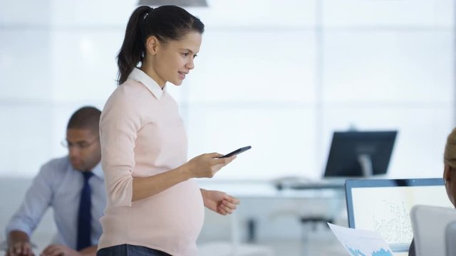  Pregnant business manager talking on the phone & overseeing staff in office