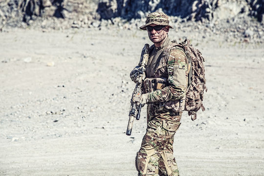 Location shot of soldier in field uniforms with rifle in the desert among rocks