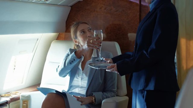  Air hostess serves champagne to businesswoman traveling on private plane
