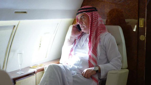  Middle Eastern businessman talking on phone while traveling by private plane