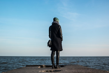 Girl with blue hair stand on sea pier looking at the sea. Shot from behind. Silhouette