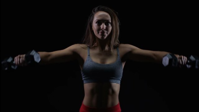  Fit woman with athletic physique lifting weights against black background