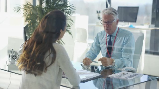  Audiology doctor talking to patient & showing her modern hi tech hearing aid