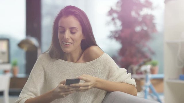  Attractive woman relaxing at home, smiling & texting on smartphone
