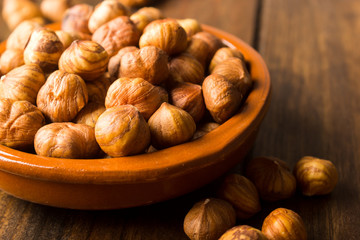 Close up of a group of peeled hazelnuts in a bowl on a wooden table.