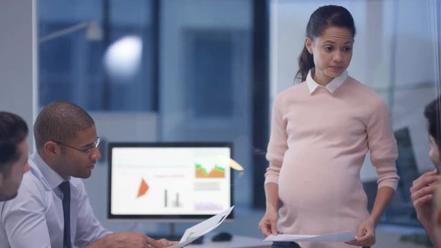  Pregnant businesswoman in a meeting with colleagues discussing financial data