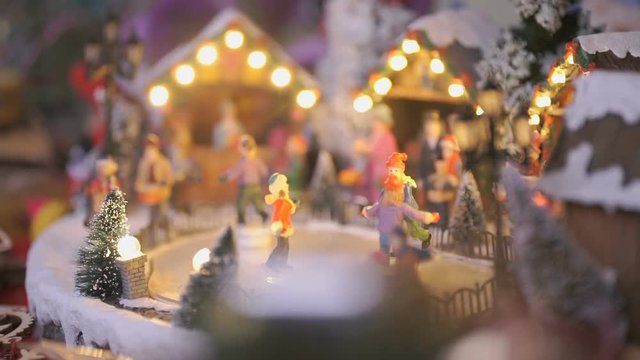 Close-up - miniature souvenir Christmas toy - little people skate in circle on an ice rink illuminated with garland with winter scenery