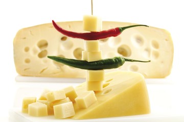 Diced cheese and hot peppers on a toothpick, half a cheese wheel in background