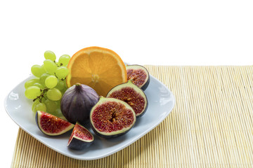 White plate with summer, juicy, sweet dietary, exotic fruits of figs, grapes, orange on a bamboo napkin.