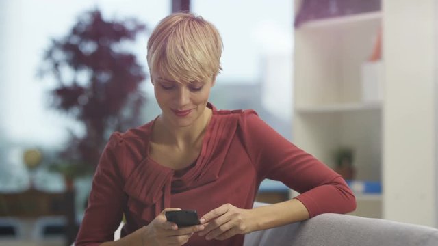  Portrait attractive woman relaxing at home, smiling & texting on smartphone.