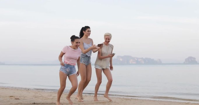 Girls Walking On Beach Holding Cell Smart Phone Laughing, Young Women Group Communication Slow Motion 60