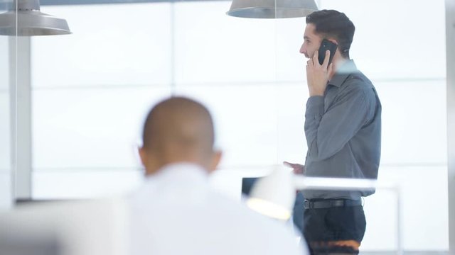  Business manager in office pacing as he talks on the phone