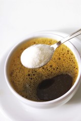 Spoonful of sugar held over a cup of coffee