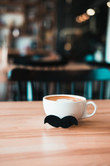 White mug of coffee with moustache on wooden table at coffee shop.  Movember event, father's day concept.