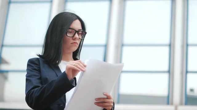 A young beautiful brunette woman in suit and glasses checks documents, utility bills. Slow motion. Businesswoman standing near office.