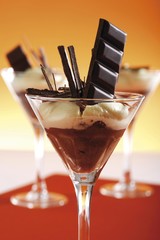 Layered chocolate mousse and vanilla mousse in glasses, garnished with chocolate shavings and a chocolate bar