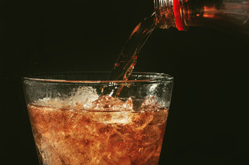 pour cola from the bottle to glass and bubble soda on black background