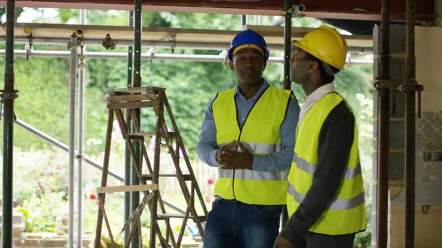  Builders working at construction site with female architect looking at plans