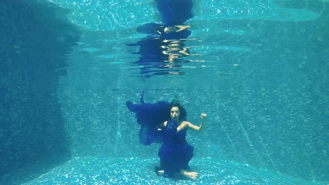 Beautiful girl in blue dress meditating under water in swimming pool