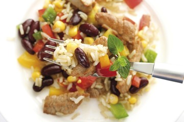 Rice dish with pork, peppers, kidney beans, corn, and long-grain rice, food on fork, bird's-eye view