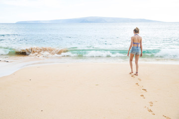 Teenage girl walking alone towards tropical island ocean on beach