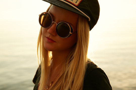 Portrait of a girl in sunset in contra light on the beach at the sea in sunglasses and baseball cap