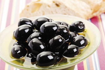Black olives and white bread on a glass plate