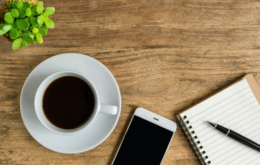 Flat lay of wood office desk with hot coffee, smartphone, eyeglasses and notebook.  Top view of minimal office desk style with copy space