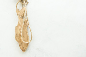 Large wooden fish with rope hanging on the white concrete wall background.