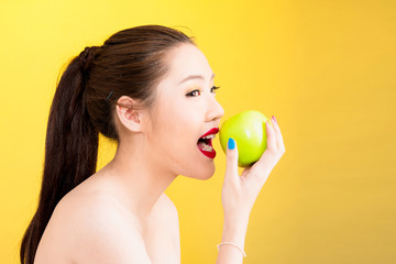 Obraz na płótnie Canvas Young Asian woman biting apple isolated in yellow background