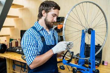 Repairman in gloves and uniform tightening hubs of bicycle wheel