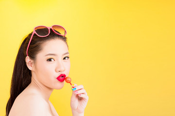 Young Asian woman kissing lollipop isolated on yellow background.