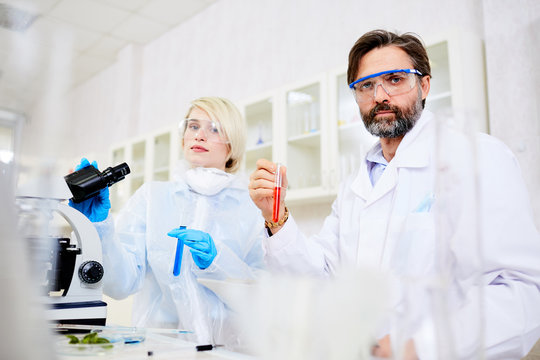 Group portrait of hard-working scientists posing for photography while carrying out experiment at modern laboratory, they wearing safety goggles