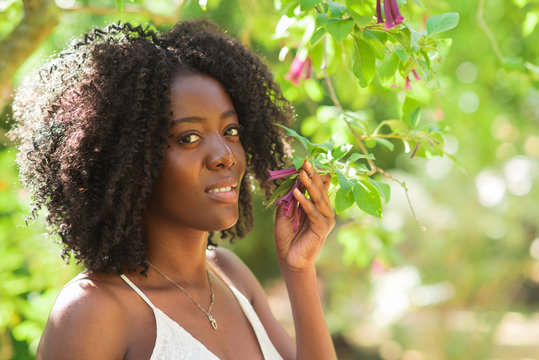 Smiling Black Woman Smelling Flowers In Park