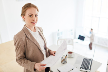 Young successful economist with papers looking at camera in office