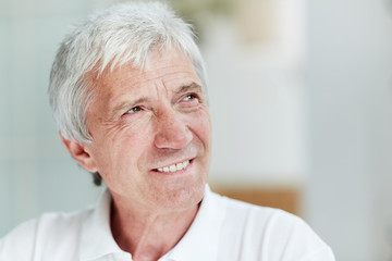 Headshot of handsome senior man looking away with warm toothy smile, blurred background