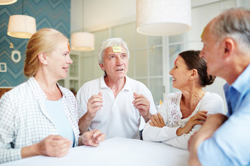 Obraz premium Group of aged friends enjoying each others company while gathered together at cozy living room with stylish design and playing guessing game