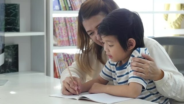 Asian mother helping her son doing homework on white table slow motion 