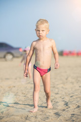 Baby boy walking on the sandy beach near the sea. Cute little kid at sand tropical beach. Ocean coast.