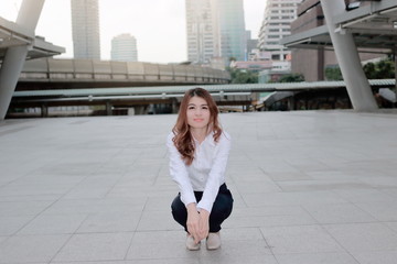 Portrait of happy young Asian woman posing in a squatting position on sidewalk at urban city background.