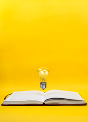 Light bulb levitating above the notebook as a concept of new idea, copyspace, yellow background.