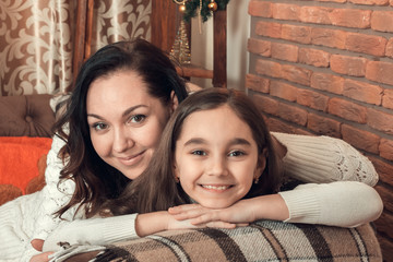 Two beautiful girls, mother and daughter siting on a sofa in Christmas decorated room.