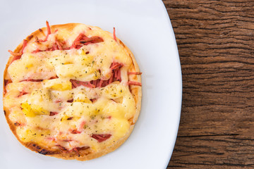 Pizza with bacon and mushrooms on white dish on wood table.