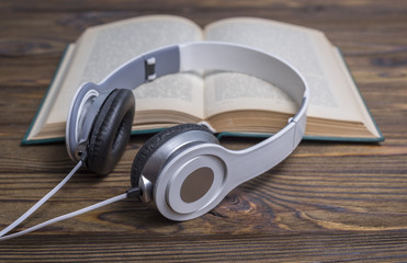 Audio book concept. Headphones and old book over wooden table.