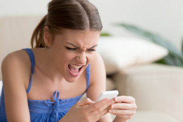 Angry young woman holding cell annoyed by not working smartphone, furious teen girl having problem...