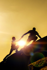 The joint work teamwork of two people man and girl travelers help each other on top of a mountain climbing team, a beautiful sunset landscape. The silhouettes on top of a mountain