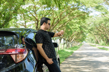 Muslim casual business man leaning against car door and look at his watch on roadside with tree and shade